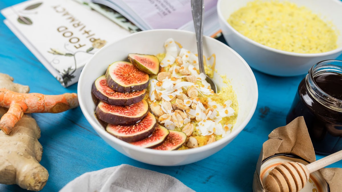 Healthy breakfast bowl with figs, nuts, and turmeric on a blue table with ginger and honey.